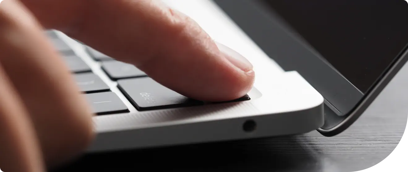 Close-up of a person pressing a fingerprint sensor on a laptop keyboard to unlock or power on the device.