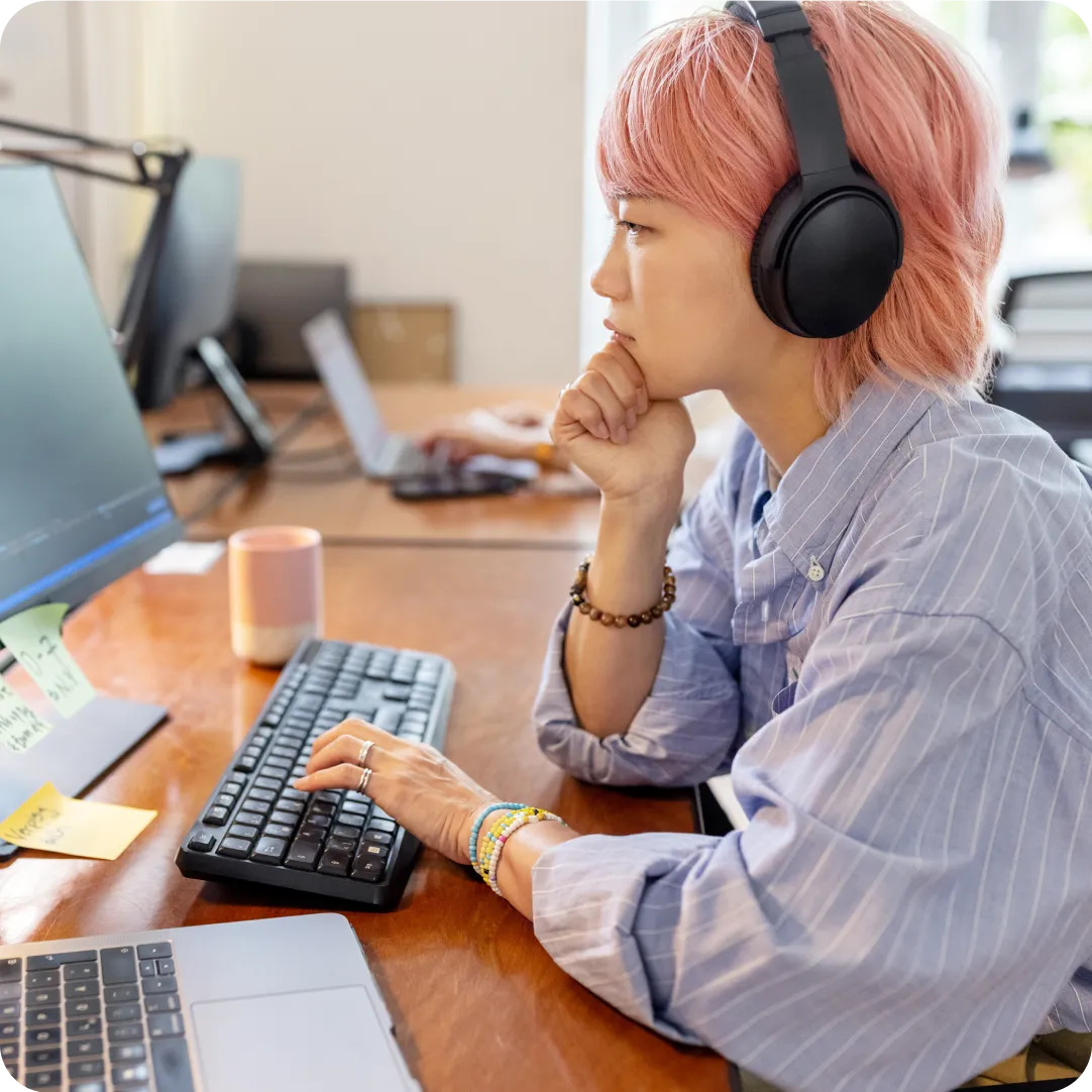 Woman wearing headphones working on a trusted device desktop computer using identity intelligence completing a security assessment.