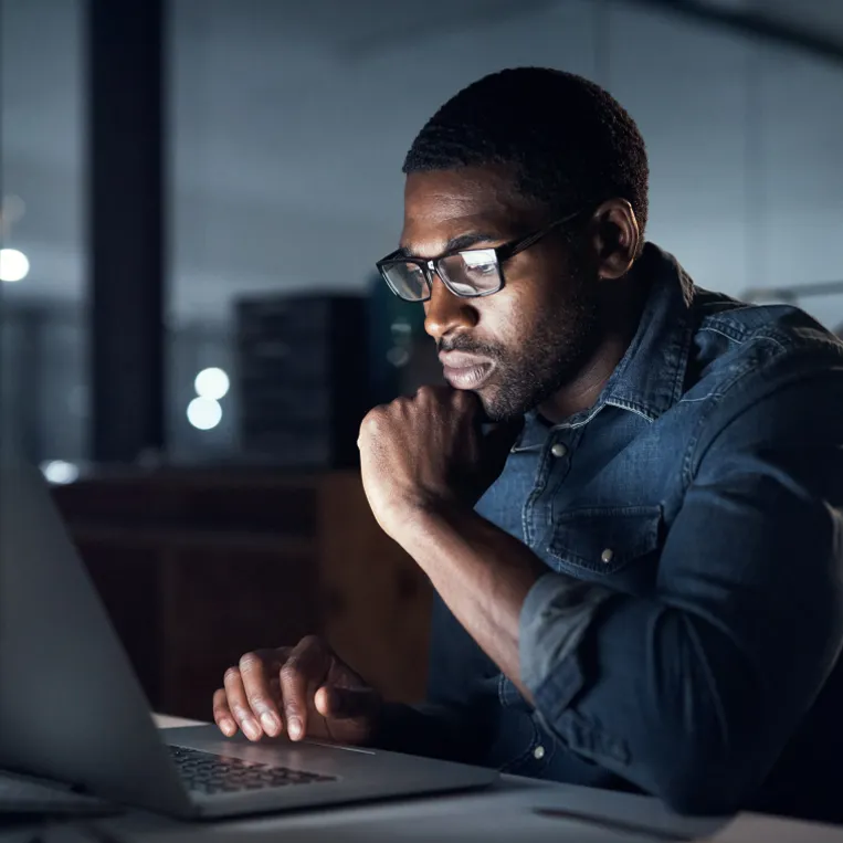 Man works on his laptop computer in a dimly lit office during the evening.